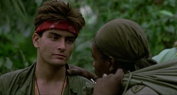 Movie still from “Platoon” (1986), directed by Oliver Stone – A man with a bandanna around his head and a woman with a cigarette in her mouth; Close Up shot, Over the shoulder angle
