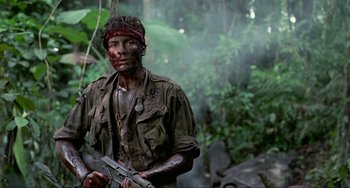 Movie still from “Platoon” (1986), directed by Oliver Stone – A man with a red bandage on his head holding a gun; Medium shot, Low angle