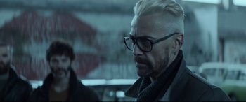 Movie still from “Atomic Blonde” (2017), directed by David Leitch – A man with white hair and glasses looking to his left; Close Up shot, Over the shoulder angle