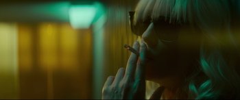 Movie still from “Atomic Blonde” (2017), directed by David Leitch – A woman smoking a cigarette in a dark room; Close Up shot, Over the shoulder angle
