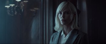 Movie still from “Atomic Blonde” (2017), directed by David Leitch – A woman with blonde hair is standing by a window; Close Up shot, Over the shoulder angle