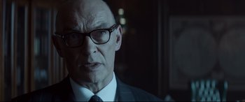 Movie still from “Atomic Blonde” (2017), directed by David Leitch – An older man wearing a suit and glasses; Close Up shot, Over the shoulder angle
