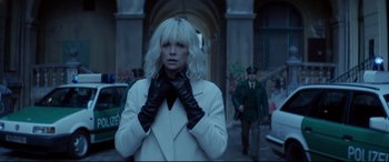 Movie still from “Atomic Blonde” (2017), directed by David Leitch – A woman in a white coat and black gloves; Medium shot, Over the shoulder angle