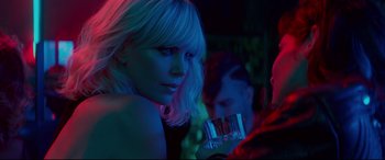 Movie still from “Atomic Blonde” (2017), directed by David Leitch – A woman with blonde hair is holding a drink; Close Up shot, Over the shoulder angle