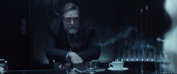 Movie still from “Atomic Blonde” (2017), directed by David Leitch – An older man sitting at a table in a dark room; Medium shot, Over the shoulder angle
