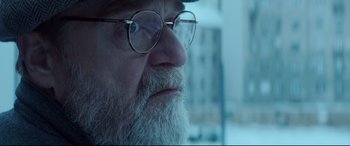 Movie still from “Atomic Blonde” (2017), directed by David Leitch – An old man with a beard wearing glasses and a hat; Close Up shot, Over the shoulder angle