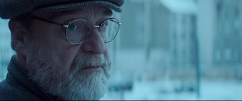 Movie still from “Atomic Blonde” (2017), directed by David Leitch – An old man with a beard wearing glasses and a hat; Close Up shot, Over the shoulder angle