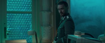 Movie still from “Atomic Blonde” (2017), directed by David Leitch – A man in a uniform standing next to a table; Medium shot, Over the shoulder angle