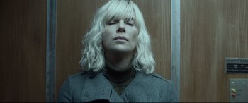 Movie still from “Atomic Blonde” (2017), directed by David Leitch – A woman with blonde curly hair and a gray jacket; Close Up shot, Low angle