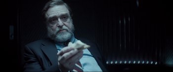Movie still from “Atomic Blonde” (2017), directed by David Leitch – An older man sitting down eating a piece of pizza; Close Up shot, Over the shoulder angle