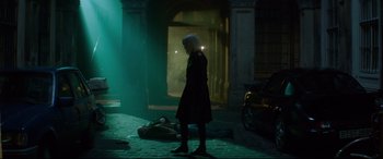 Movie still from “Atomic Blonde” (2017), directed by David Leitch – A woman standing on the sidewalk next to a person laying on the ground; Wide shot, Over the shoulder angle