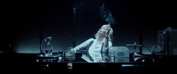 Movie still from “Atomic Blonde” (2017), directed by David Leitch – A woman sitting at a table smoking a cigarette in front of a mirror; Medium shot, Low angle