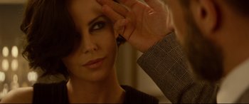 Movie still from “Atomic Blonde” (2017), directed by David Leitch – A woman looking into a mirror while holding her hand up to her face; Close Up shot, Over the shoulder angle