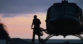 Movie still from “Predator” (1987), directed by John McTiernan – A man standing next to a helicopter on a beach; Wide shot, Low angle
