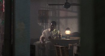 Movie still from “Predator” (1987), directed by John McTiernan – A man sitting at a table with a glass of beer; Medium shot, Low angle