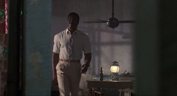 Movie still from “Predator” (1987), directed by John McTiernan – A man standing in front of a table holding a knife; Wide shot, Low angle