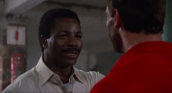 Movie still from “Predator” (1987), directed by John McTiernan – Two men talking to each other in front of a brick wall; Close Up shot, Over the shoulder angle