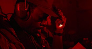 Movie still from “Predator” (1987), directed by John McTiernan – A man wearing headphones and holding a cell phone in his hand; Close Up shot, Low angle