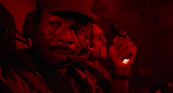 Movie still from “Predator” (1987), directed by John McTiernan – A man in a hat is holding a cell phone; Close Up shot, Low angle
