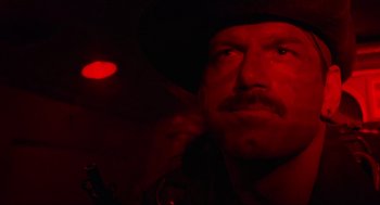 Movie still from “Predator” (1987), directed by John McTiernan – A person wearing a hat in a dark room; Close Up shot, Low angle