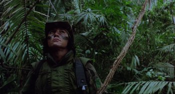 Movie still from “Predator” (1987), directed by John McTiernan – A man in a camouflage outfit standing in the woods; Medium shot, Low angle