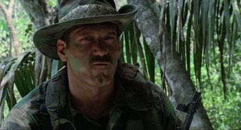 Movie still from “Predator” (1987), directed by John McTiernan – A person wearing a hat near a tree; Close Up shot, Low angle