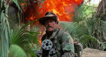 Movie still from “Predator” (1987), directed by John McTiernan – A man in a hat and a camouflage outfit; Medium shot, Low angle