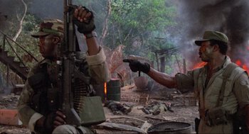 Movie still from “Predator” (1987), directed by John McTiernan – A man pointing at a man holding a gun; Medium shot, Low angle