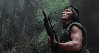 Movie still from “Predator” (1987), directed by John McTiernan – A man holding a rifle in the woods; Medium shot, Low angle