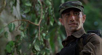 Movie still from “Predator” (1987), directed by John McTiernan – A man wearing a camouflage hat and a black shirt; Close Up shot, Low angle