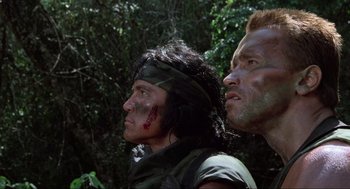Movie still from “Predator” (1987), directed by John McTiernan – Two men in the woods looking into the distance; Close Up shot, Low angle