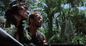 Movie still from “Predator” (1987), directed by John McTiernan – Two men are standing next to each other in the woods; Medium shot, Low angle