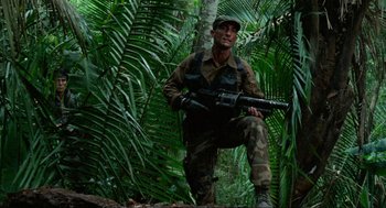 Movie still from “Predator” (1987), directed by John McTiernan – A man with a gun in the woods; Medium shot, Low angle