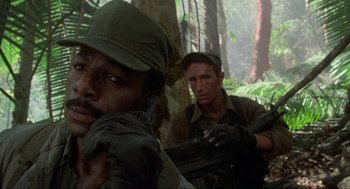 Movie still from “Predator” (1987), directed by John McTiernan – Two men in the woods , one of whom is holding a gun; Close Up shot, Low angle
