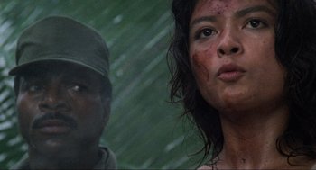 Movie still from “Predator” (1987), directed by John McTiernan – A man and a woman are standing next to each other; Close Up shot, Low angle