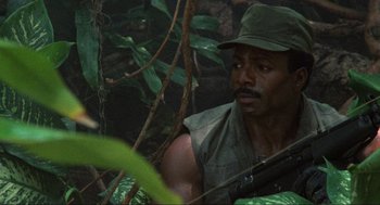 Movie still from “Predator” (1987), directed by John McTiernan – A man with a rifle in the jungle; Close Up shot, Low angle