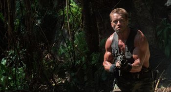 Movie still from “Predator” (1987), directed by John McTiernan – A man with a gun standing in the woods; Medium shot, Low angle