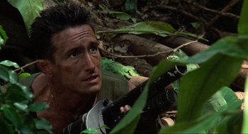 Movie still from “Predator” (1987), directed by John McTiernan – A person holding a rifle in the woods; Close Up shot, Low angle