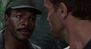 Movie still from “Predator” (1987), directed by John McTiernan – Two men talking to each other in front of a brick wall; Close Up shot, Over the shoulder angle