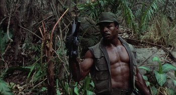 Movie still from “Predator” (1987), directed by John McTiernan – A man holding a gun while standing in the woods; Medium shot, Low angle