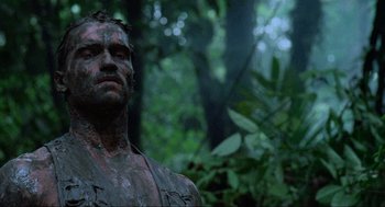 Movie still from “Predator” (1987), directed by John McTiernan – A person with mud all over his face; Close Up shot, Low angle