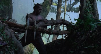 Movie still from “Predator” (1987), directed by John McTiernan – A man is carrying a tree branch in the woods; Wide shot, Low angle