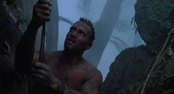 Movie still from “Predator” (1987), directed by John McTiernan – A shirtless man holding onto a pole in the jungle; Close Up shot, Low angle