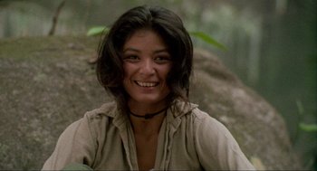 Movie still from “Predator” (1987), directed by John McTiernan – A woman smiling for the camera in the woods; Close Up shot, Low angle
