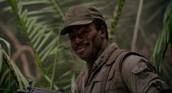 Movie still from “Predator” (1987), directed by John McTiernan – A man wearing a hat standing next to a tree; Close Up shot, Low angle
