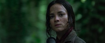 Movie still from “Predators” (2010), directed by Nimród Antal – A person holding a microphone near a forest; Close Up shot, Low angle