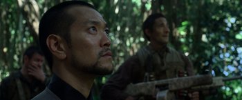 Movie still from “Predators” (2010), directed by Nimród Antal – A man looking into the distance while another man sits in the background; Close Up shot, Low angle