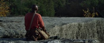 Movie still from “Predators” (2010), directed by Nimród Antal – A man sitting on the ground looking at the trees; Wide shot, Over the shoulder angle