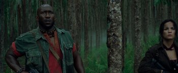 Movie still from “Predators” (2010), directed by Nimród Antal – A man standing next to a tree in the woods; Close Up shot, Low angle