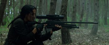 Movie still from “Predators” (2010), directed by Nimród Antal – A woman holding a rifle in a forest; Medium shot, Over the shoulder angle